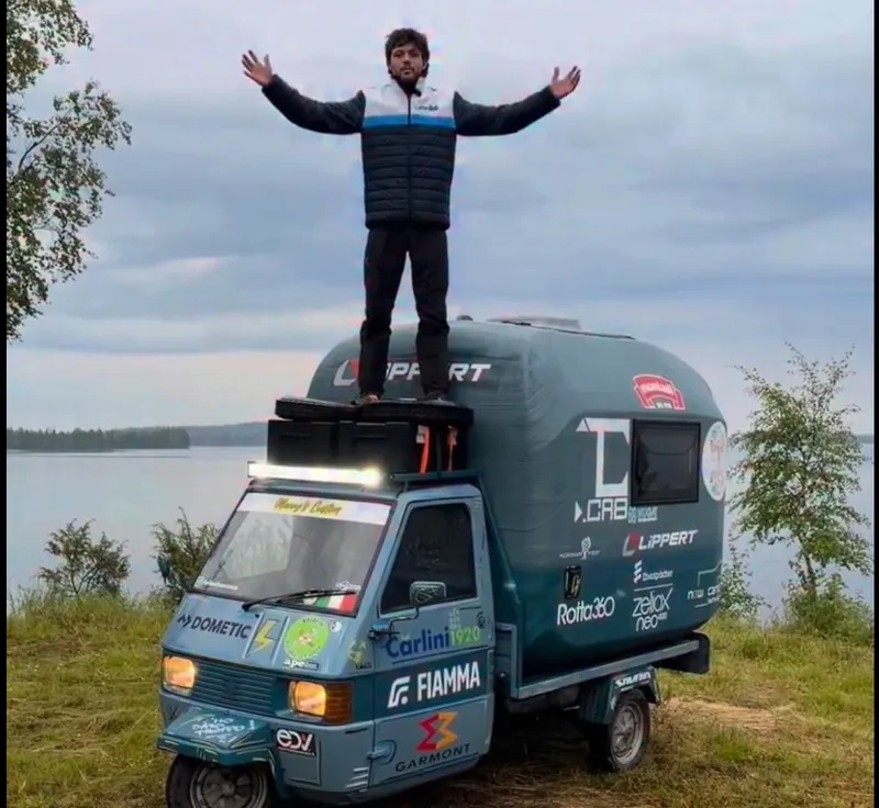 Francesco Furlani standing on the living module 3D printed by NUGAE on his Piaggio Ape TM 703, by a lake on the way to the North Cape